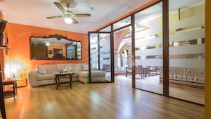 A spacious living room with a ceiling fan, a large mirror, and a view of a courtyard through glass doors. - Hotel Esmeralda (Osuna)
