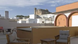 An outdoor seating area with wooden chairs and a table, overlooking a cityscape with historical buildings. - Hotel Esmeralda (Osuna)
