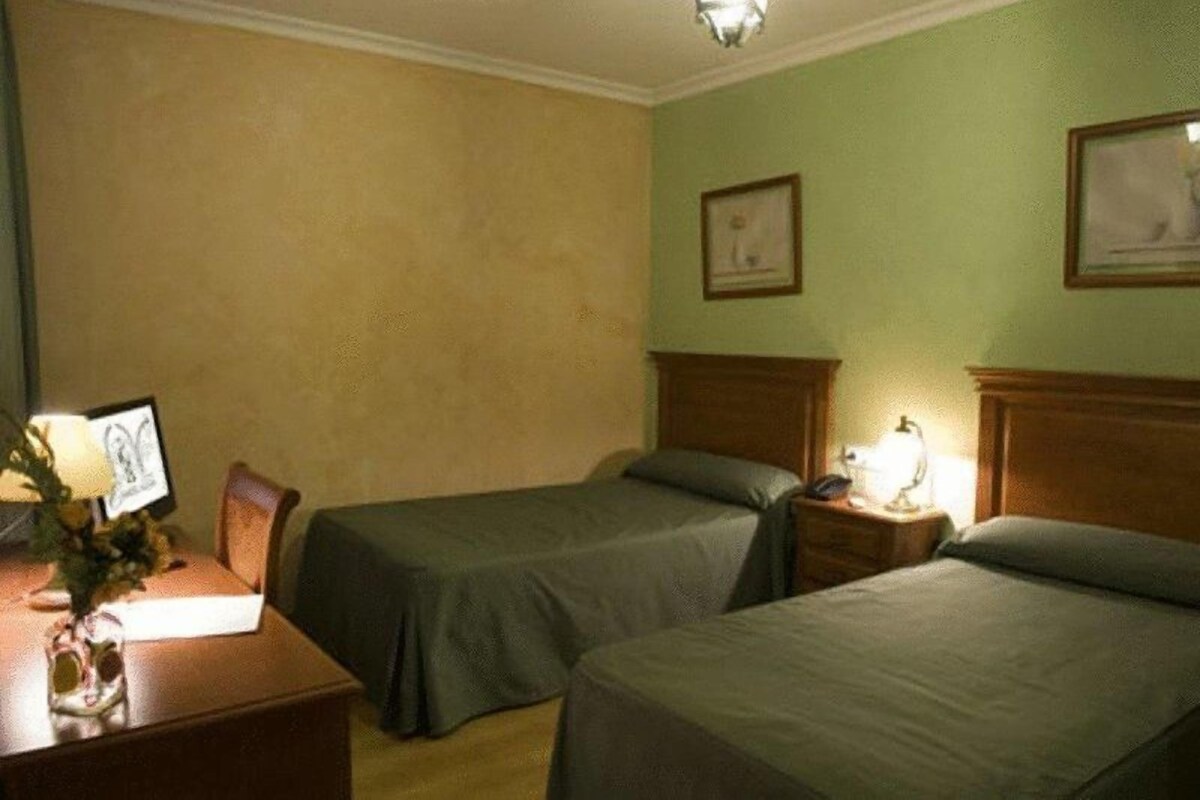 Una habitación de hotel con dos camas individuales, un escritorio con lámpara y un marco de fotos en la pared.