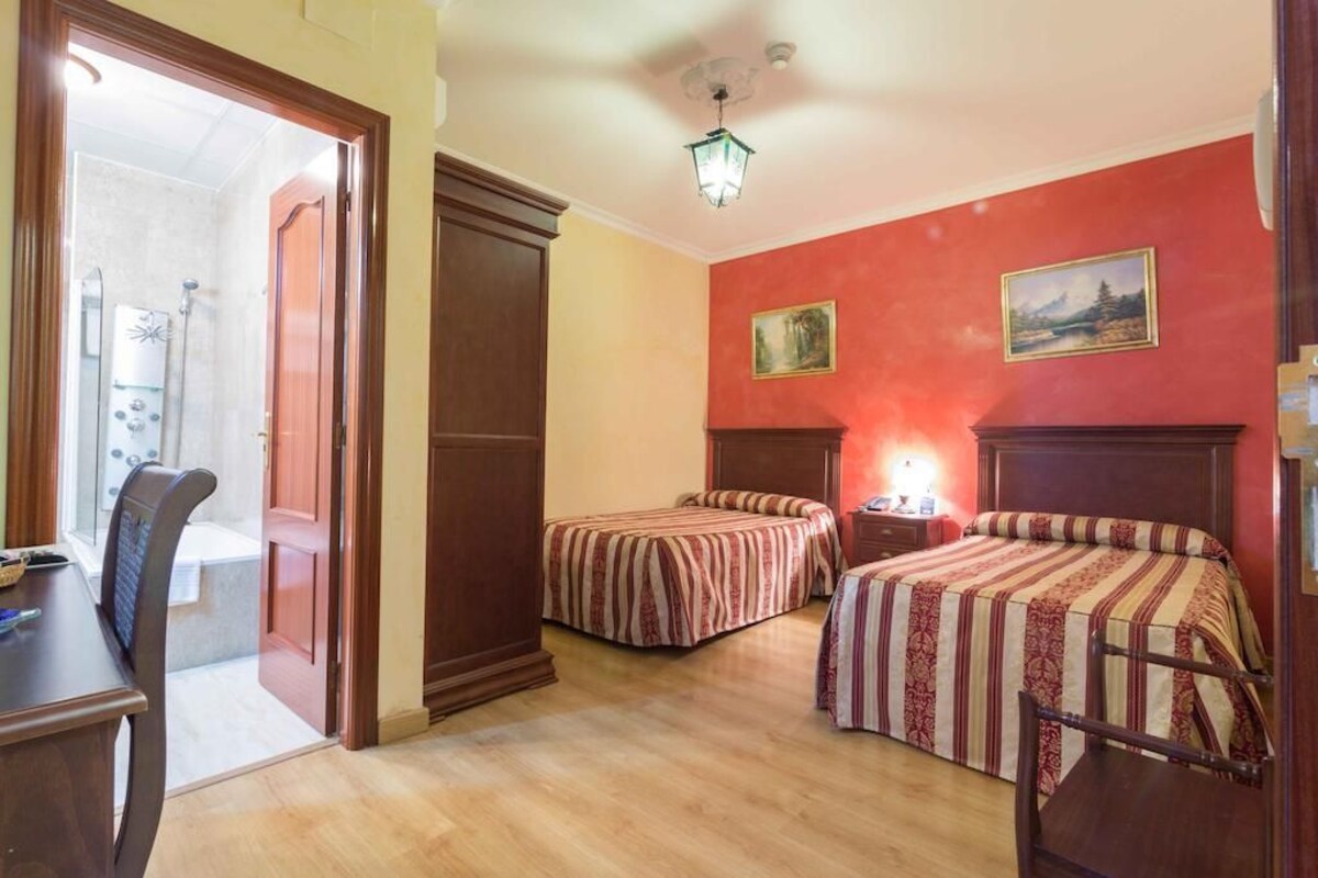 Habitación de hotel con dos camas, un escritorio y zona de ducha.