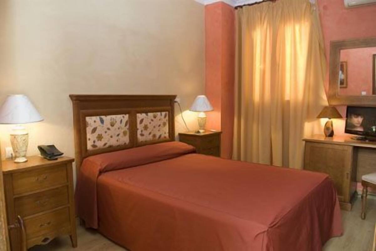 Ein Hotelzimmer mit einem Bett, zwei Nachttischen mit Lampen, einer Holzkommode und einem Schreibtisch mit Stuhl.