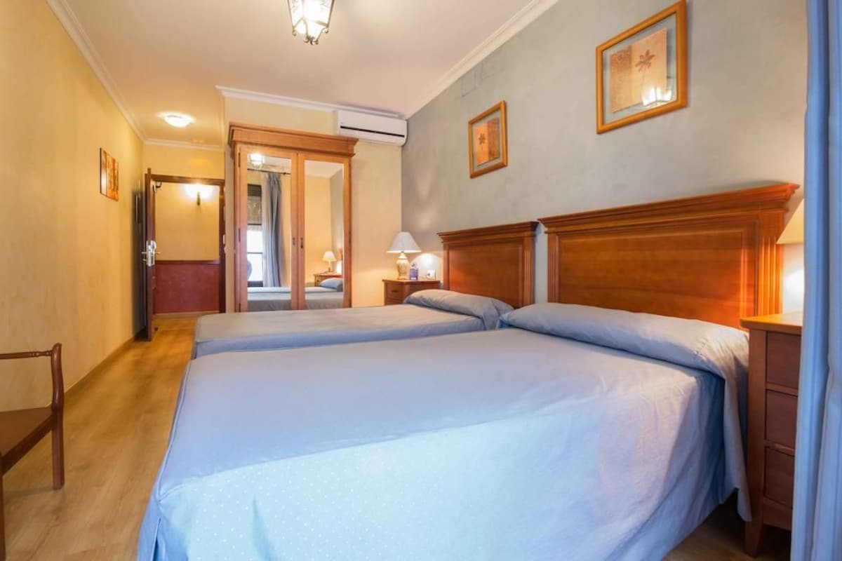 Ein Hotelzimmer mit zwei Betten, einem hölzernen Kopfteil, einem Nachttisch mit Lampe und einer Tür, die in einen anderen Raum führt.