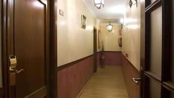 A hallway with wooden doors and walls, a carpeted floor, and wall-mounted lighting fixtures.
