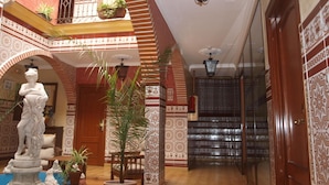 A spacious hallway with a staircase, a statue, and potted plants. - Hotel Esmeralda (Osuna)