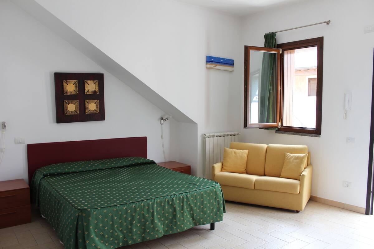 Un dormitorio con cama, sofá, ventana y radiador.