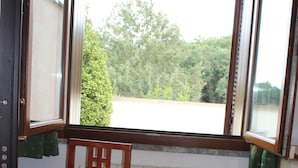 Una mesa de madera para comer con un tazón, una silla y un ventanal con cortinas.