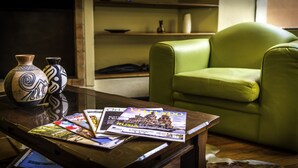 Una habitación con un sillón verde, una mesa de centro de madera con folletos de viajes y jarrones decorativos.
