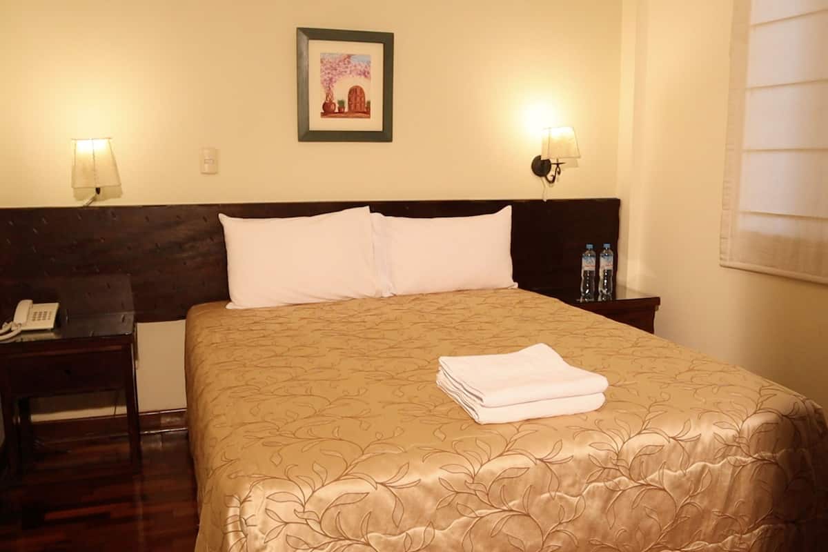 Ein Hotelzimmer mit einem Bett, zwei Nachttischlampen, einem Nachttisch mit Telefon und einem gerahmten Bild an der Wand.