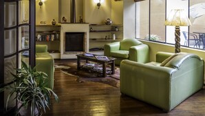 Un salón acogedor con chimenea, sofás de cuero verde, suelo de madera y un ventanal con un paraguas.