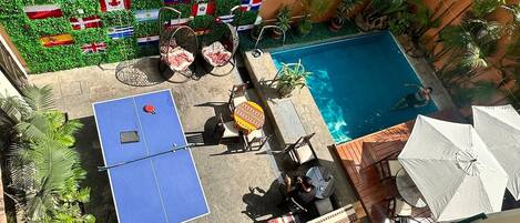 A rooftop pool area with multiple flags, a ping pong table, and outdoor seating.