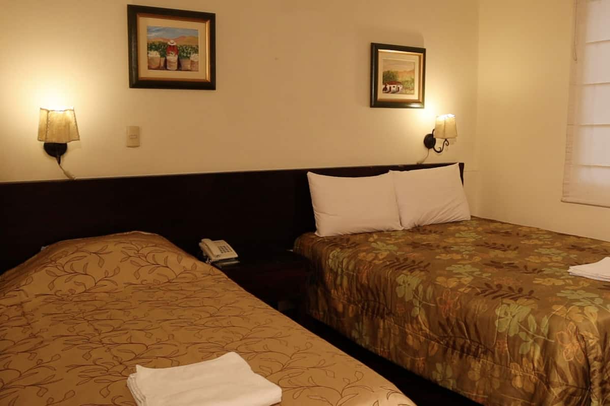 Ein Hotelzimmer mit zwei Betten, jeweils mit blumigem Bettbezug. Zwei Wandlampen, ein Telefon und zwei gerahmte Bilder schmücken die Wand.