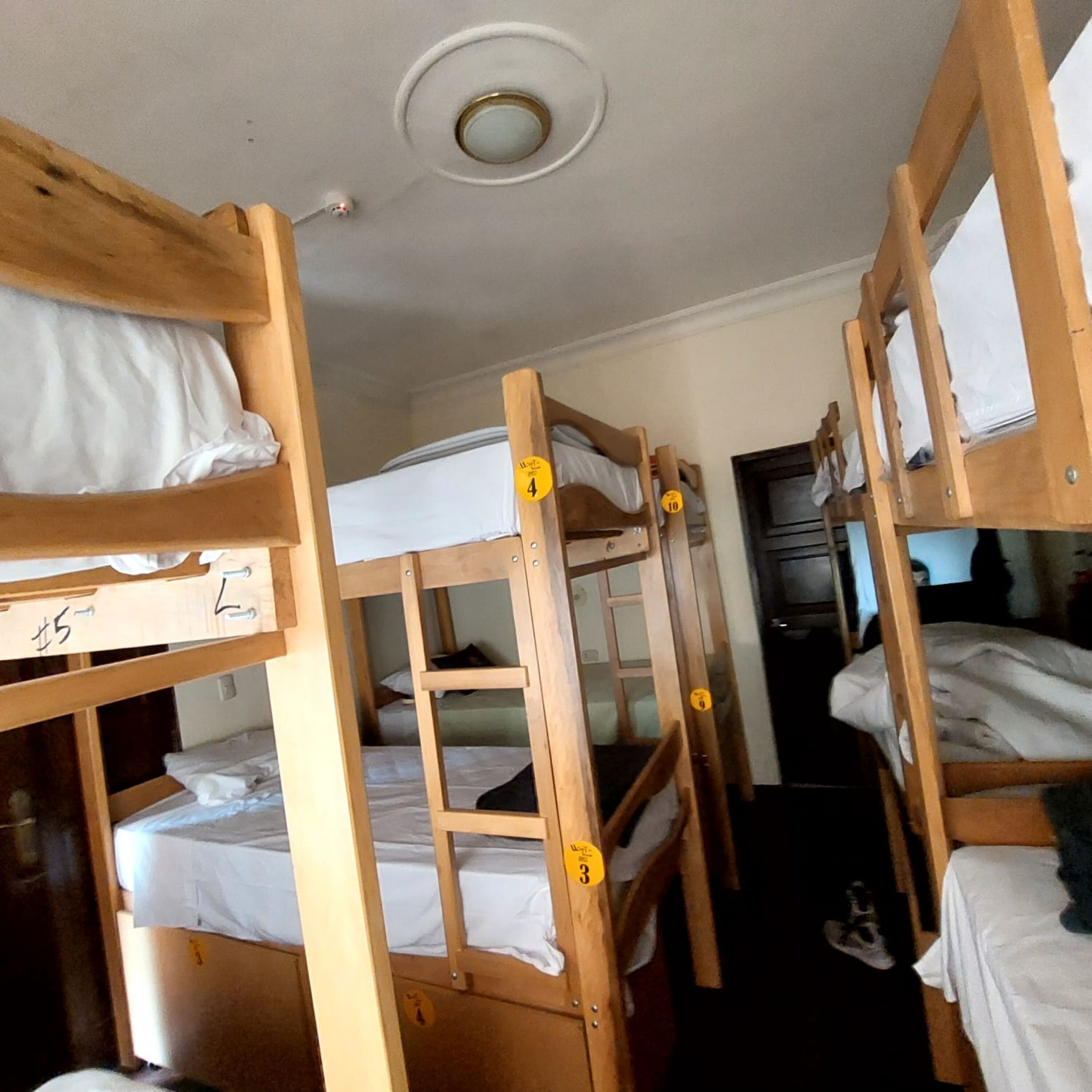 A dormitory room with bunk beds, numbered tags, and a ceiling light.