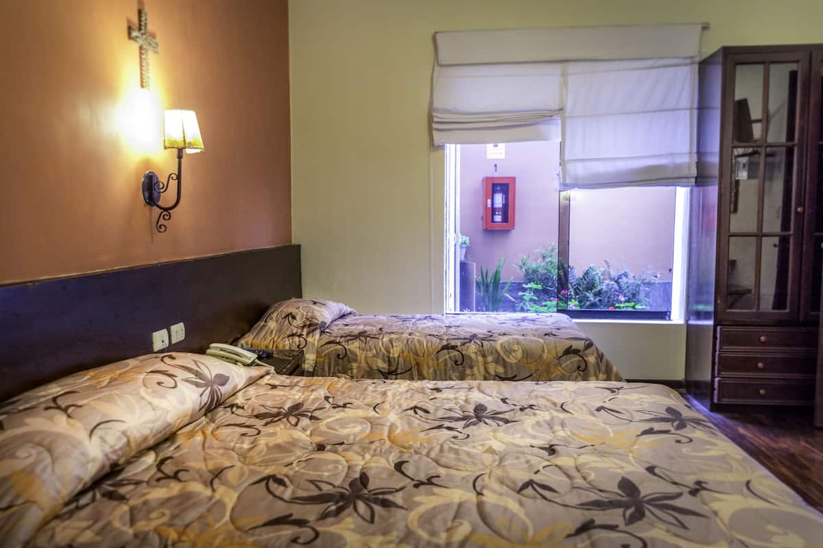 Ein Hotelzimmer mit zwei Betten, einem Nachttisch, einer Lampe, einem Fenster mit Blick ins Grüne und einem Schrank.