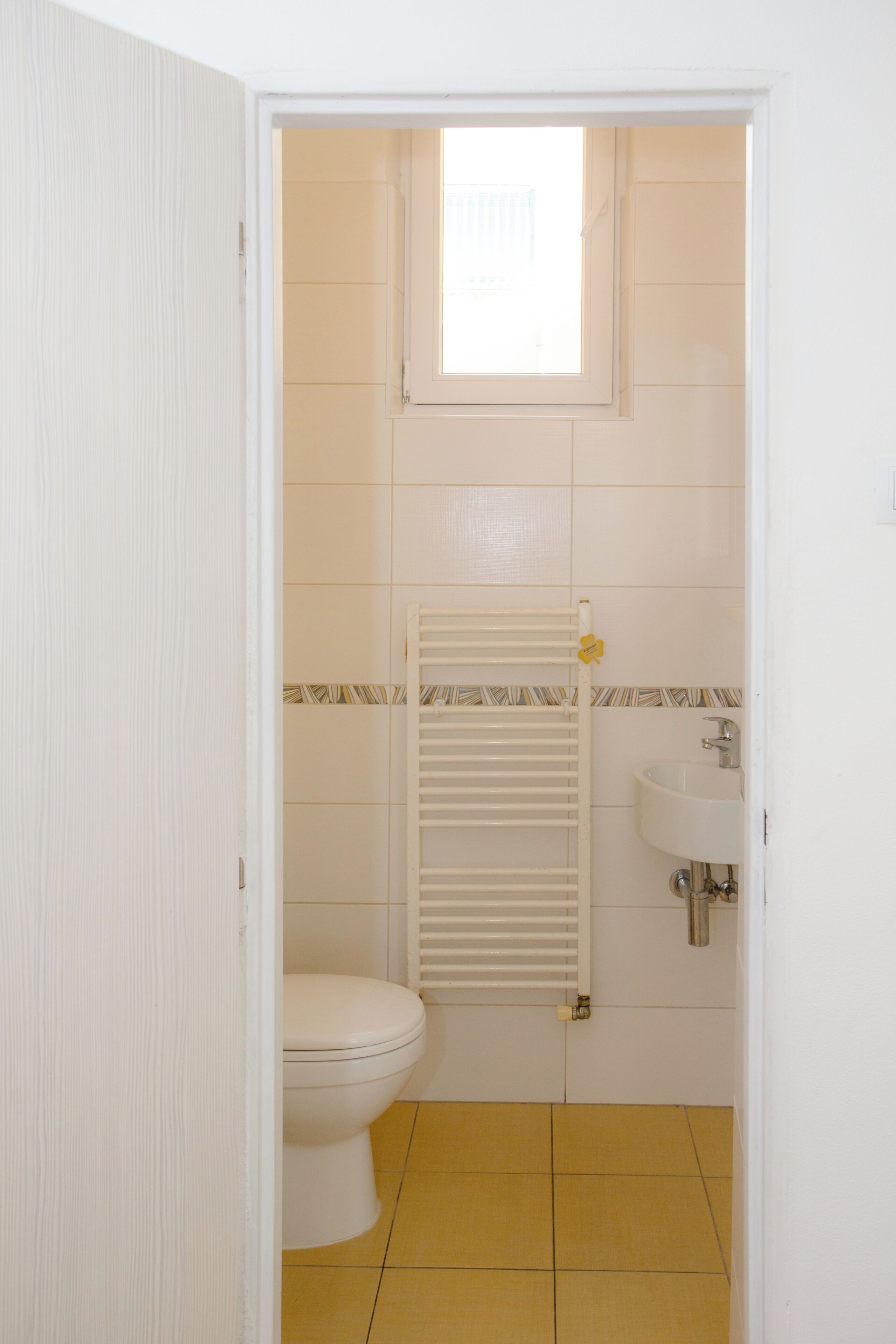 Une petite salle de bain comprenant des toilettes, un lavabo, un porte-serviettes et une fenêtre.