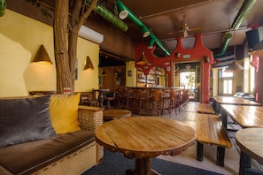Een gezellig restaurantinterieur met houten tafels, een bar en een zithoek met een bank en kussens.