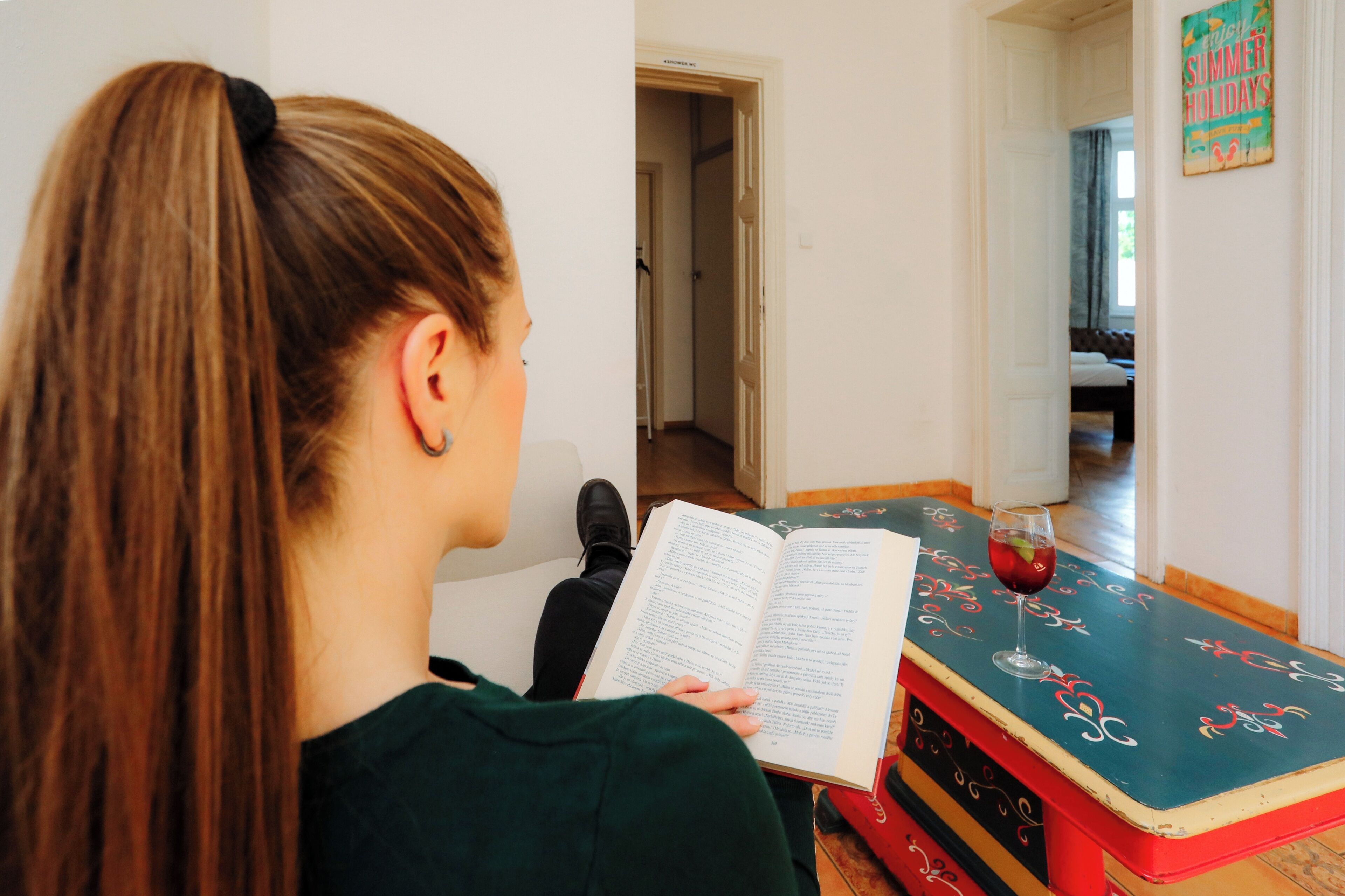 A person reading a book in a room with a door leading to another room and a wall with a sign.