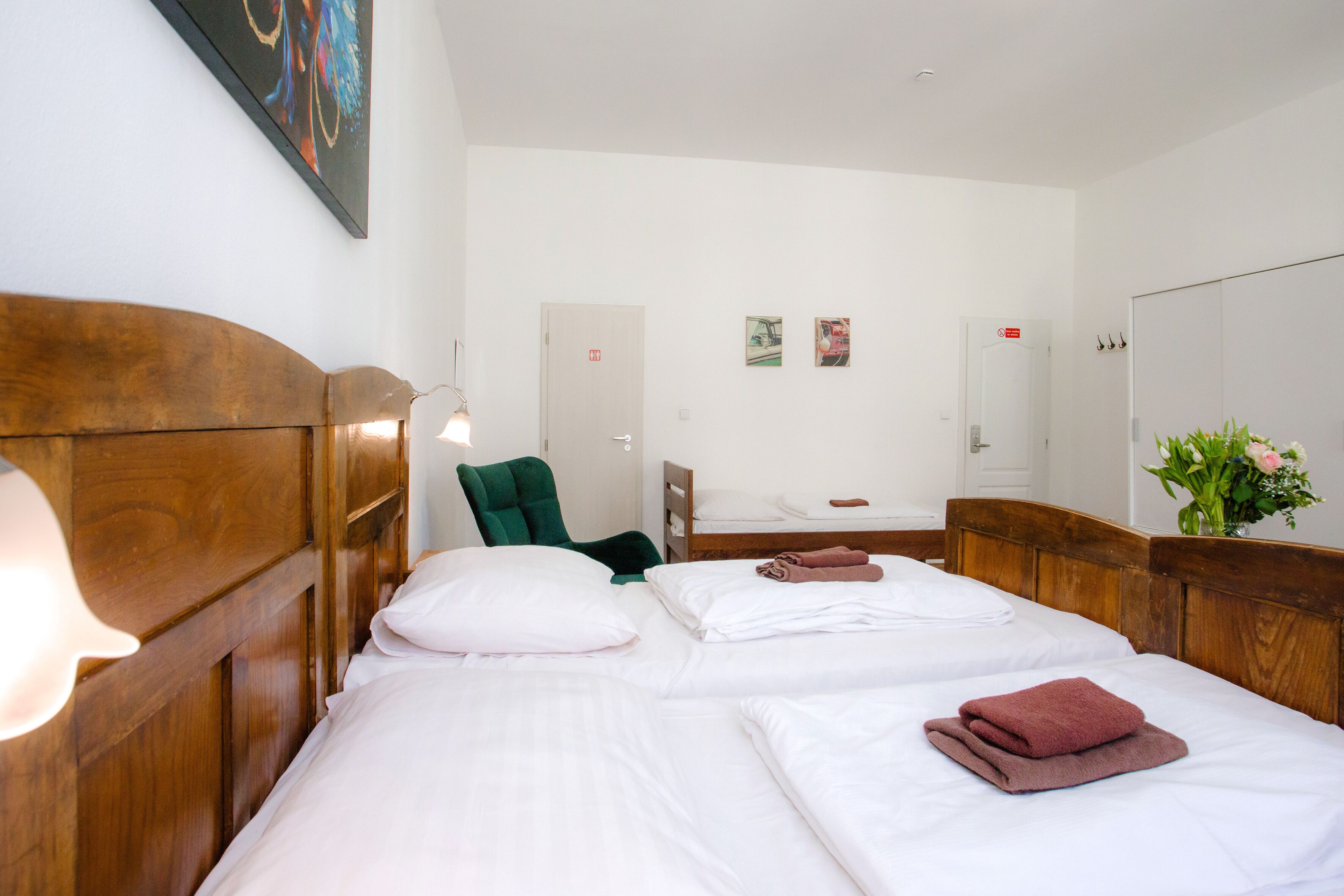Una camera d'albergo con due letti, una testiera in legno, una sedia verde, un comodino e una lampada a parete.