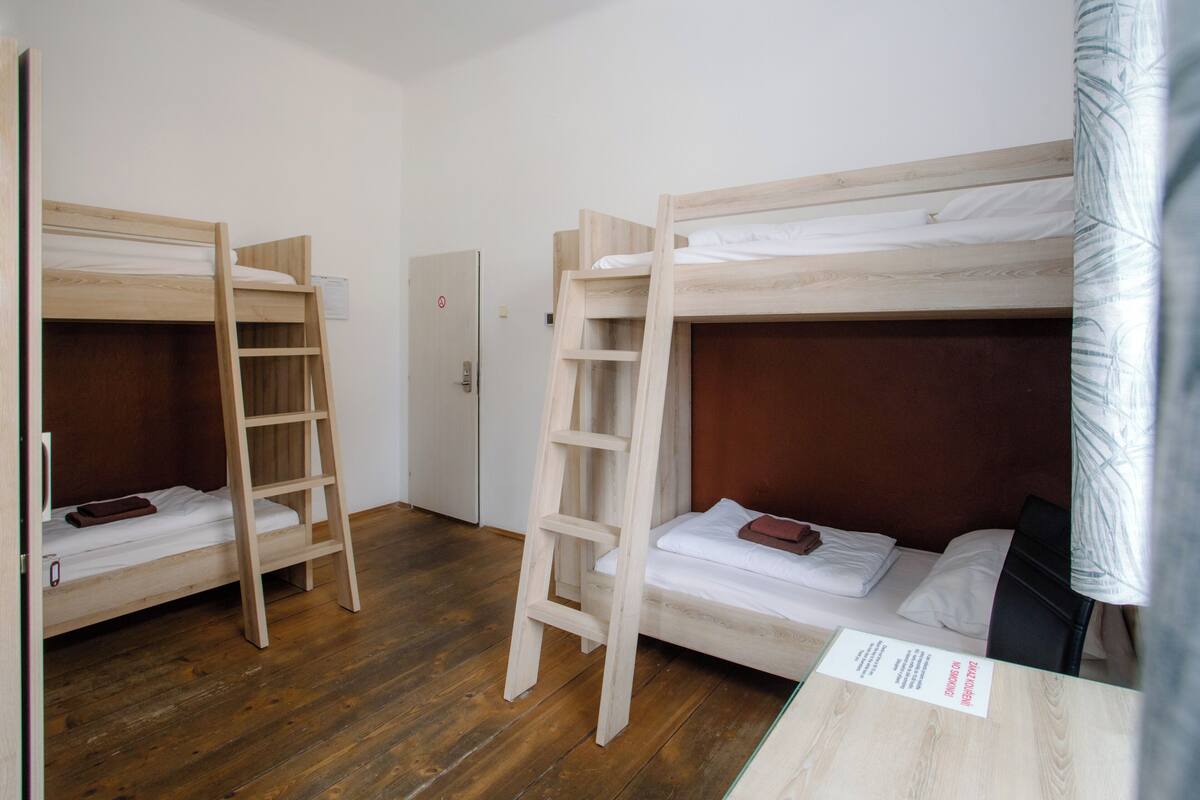 Ein Zimmer mit zwei Etagenbetten, Holzleitern, einer weißen Tür und einem Holztisch mit einer Speisekarte.