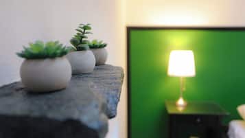 Een bed met een groene muur, een nachtkastje met een lamp en drie potplanten op een rots.