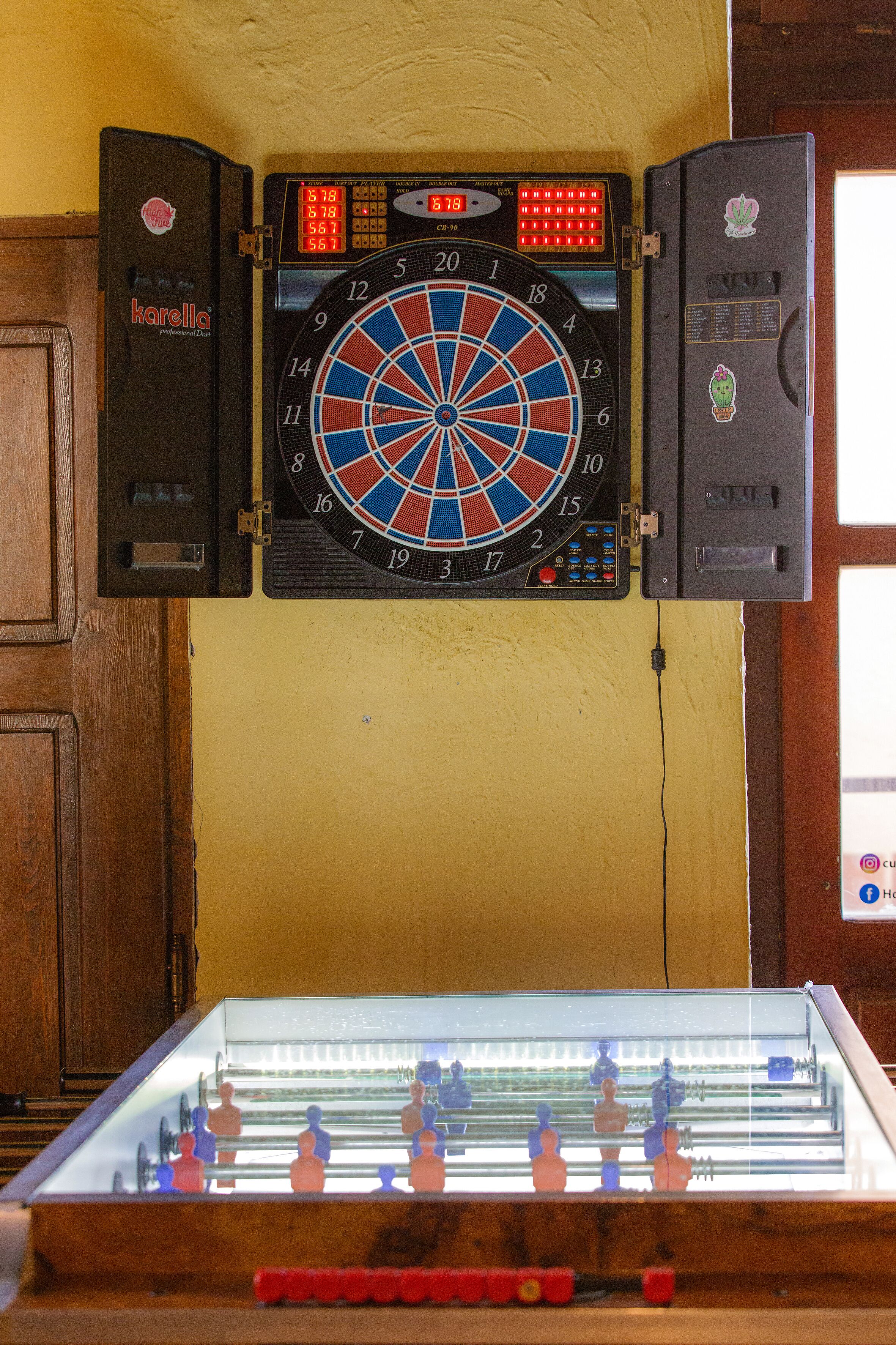 A dartboard mounted above a foosball table in a room with wooden cabinets.