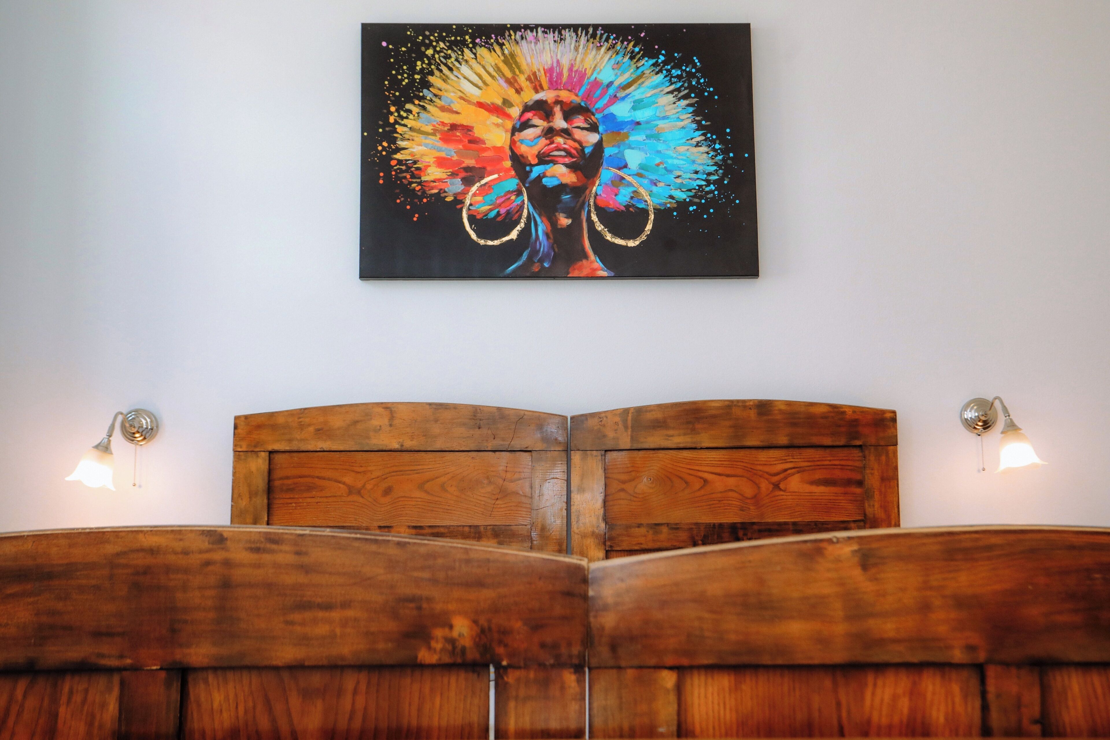 A bed with a wooden headboard, a wall-mounted painting, and two wall-mounted lamps.