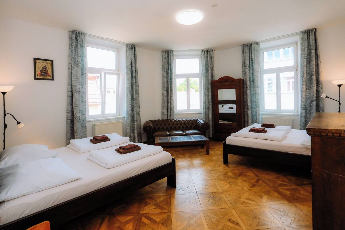 Ein Hotelzimmer mit zwei Betten, einem Sofa, einem Spiegel und Holzboden.