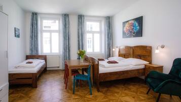 Ein Zimmer mit zwei Einzelbetten, einem Holztisch mit Stühlen, einer Blumenvase und einem Bild an der Wand.