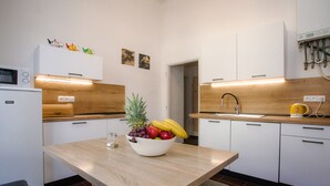 Une cuisine moderne avec des meubles blancs, un plan de travail en bois, un panier de fruits et un four à micro-ondes.