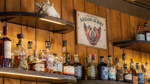 Un bar aux murs en bois, avec une affiche encadrée représentant «The Original Sailor Jerry», et diverses bouteilles d’alcool.