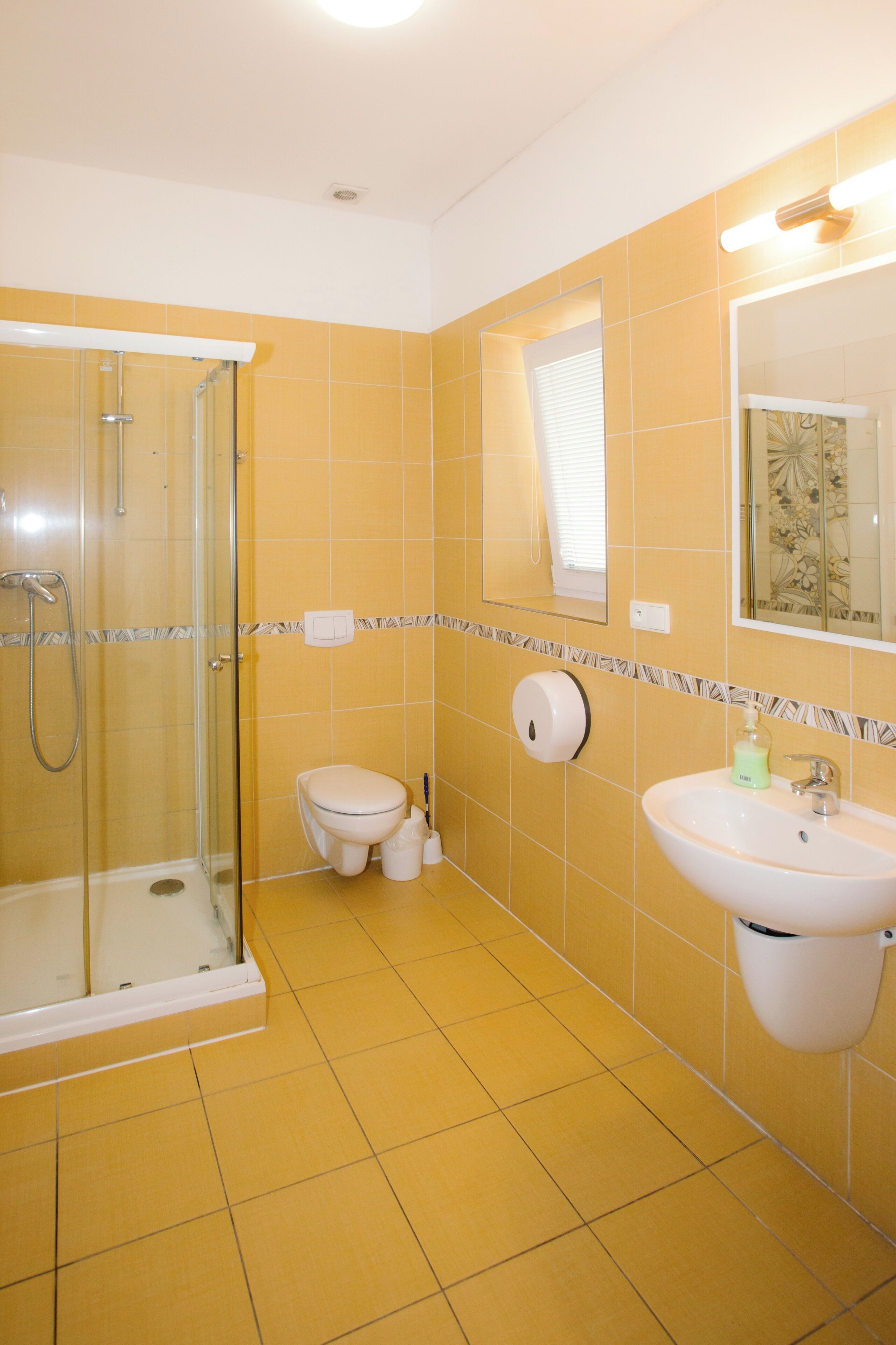 A bathroom with yellow tiles, a glass shower enclosure, a toilet, a sink, and a mirror.
