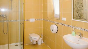 A bathroom with yellow tiles, a glass shower enclosure, a toilet, a sink, and a mirror.