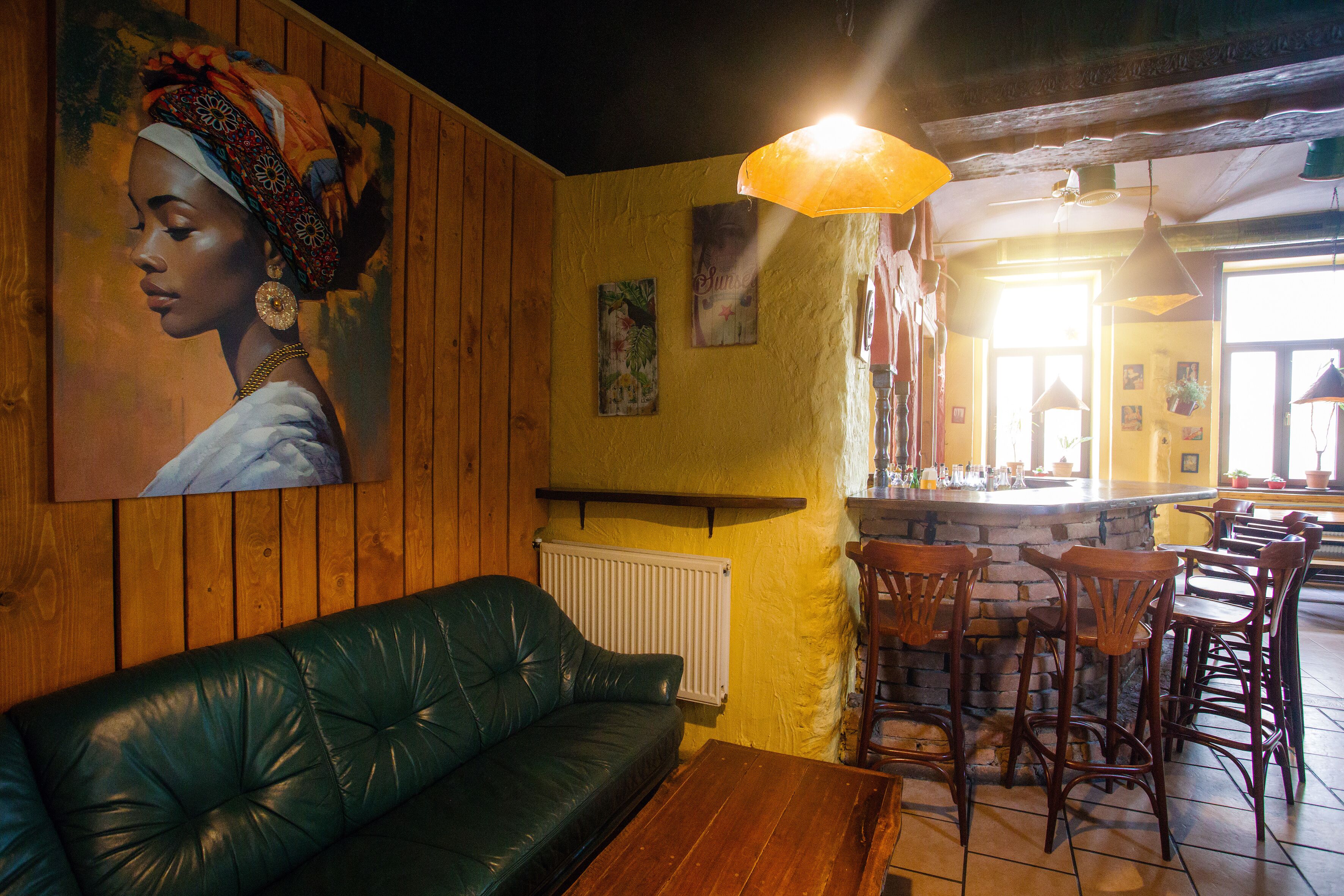 A bar area with wooden furniture, a green leather sofa, and a mural on the wall.