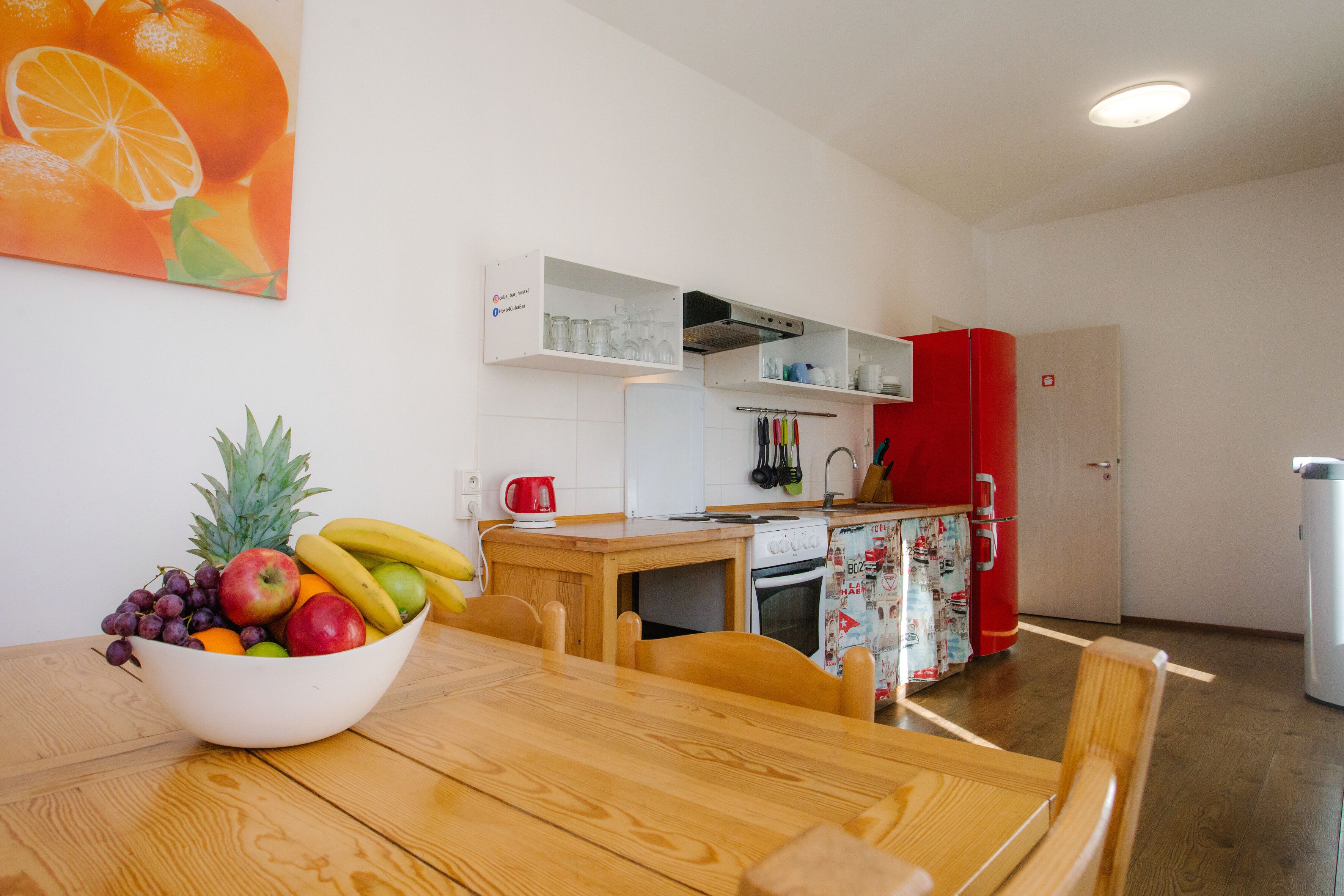 Une cuisine moderne avec des meubles blancs, un réfrigérateur rouge et une table à manger en bois, accompagnée de chaises.