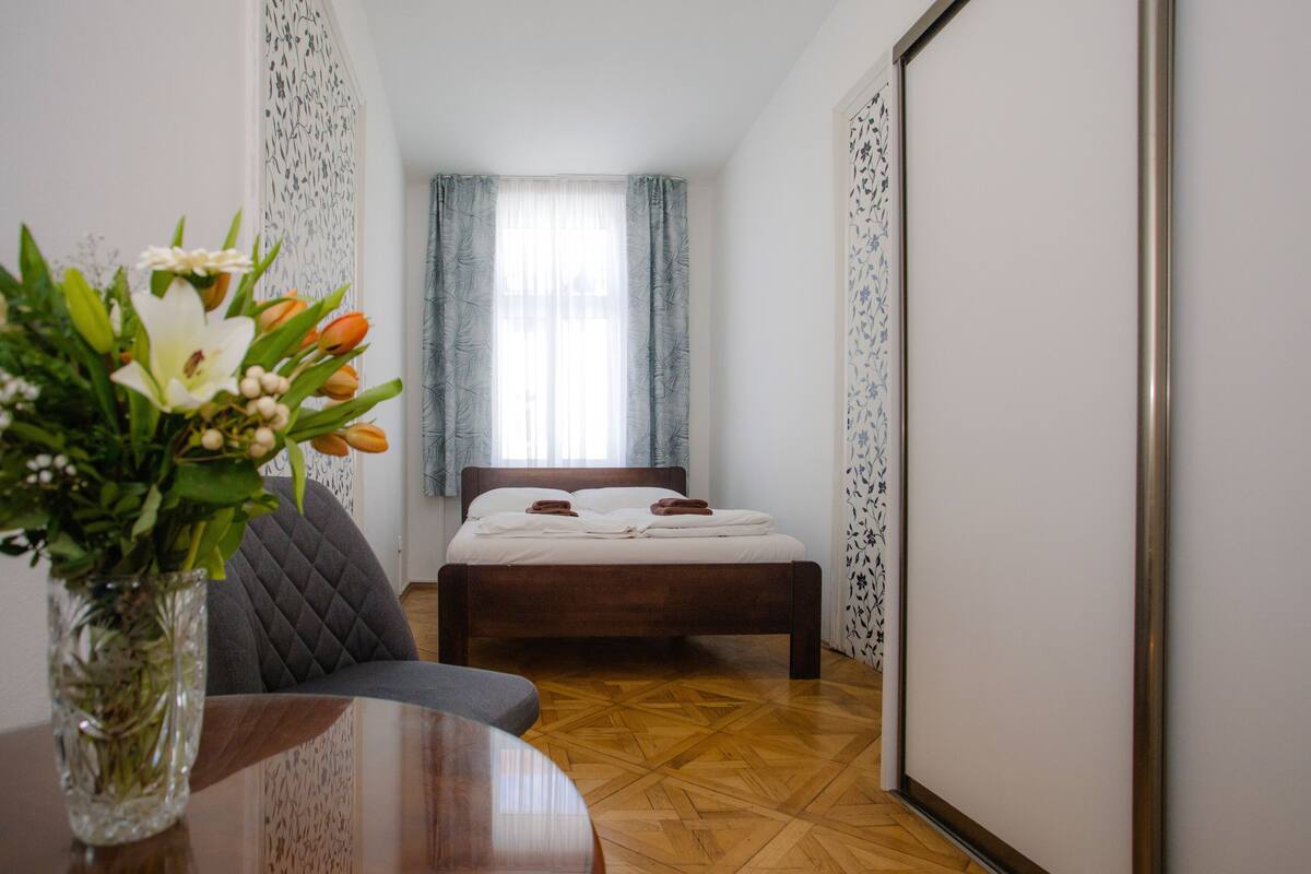Ein Schlafzimmer mit einem Bett, einem Sessel, einem Tisch und einer Blumenvase.