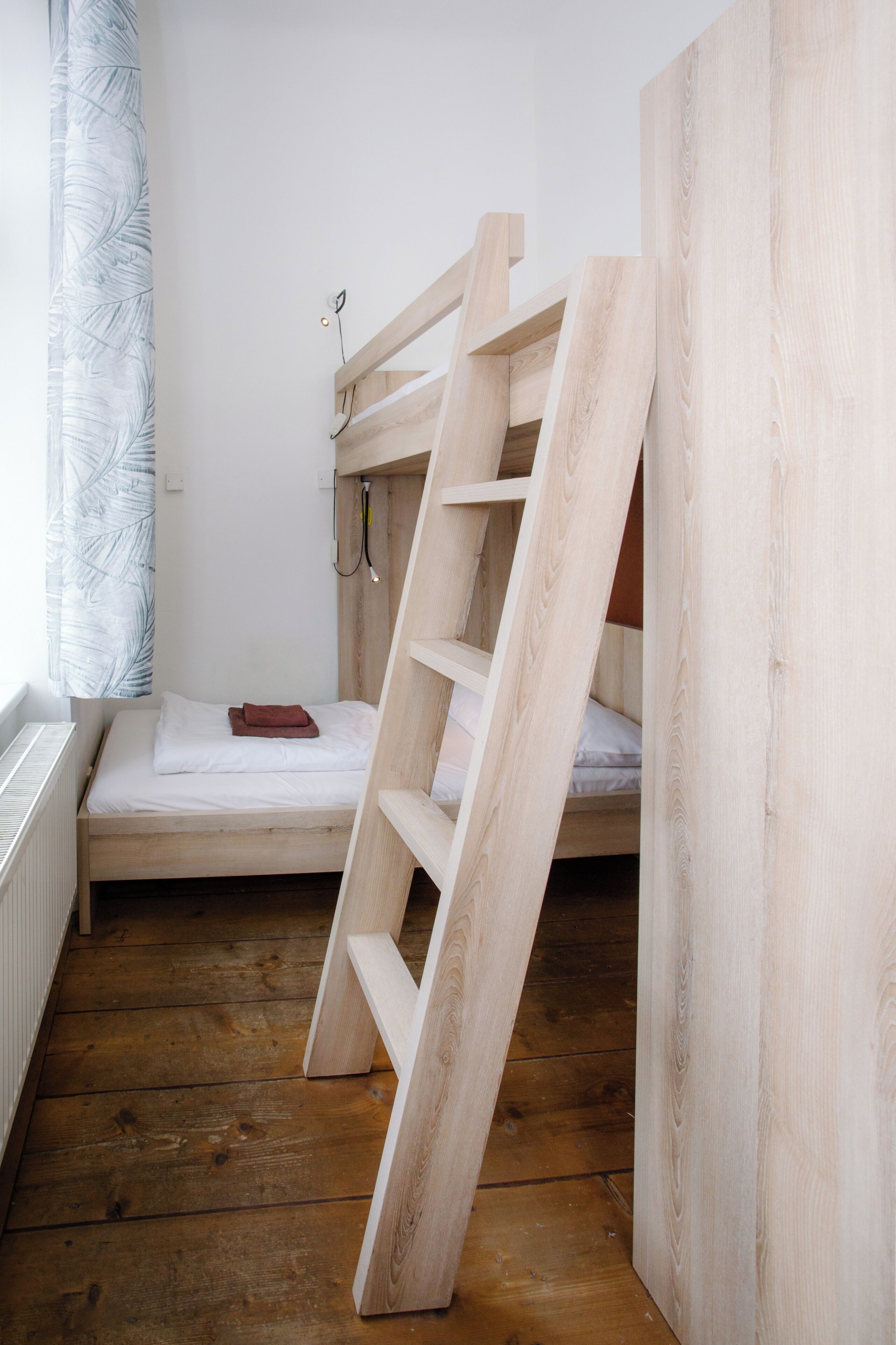 Una habitación pequeña con estructura de madera, una cama superpuesta, una escalera y un radiador.