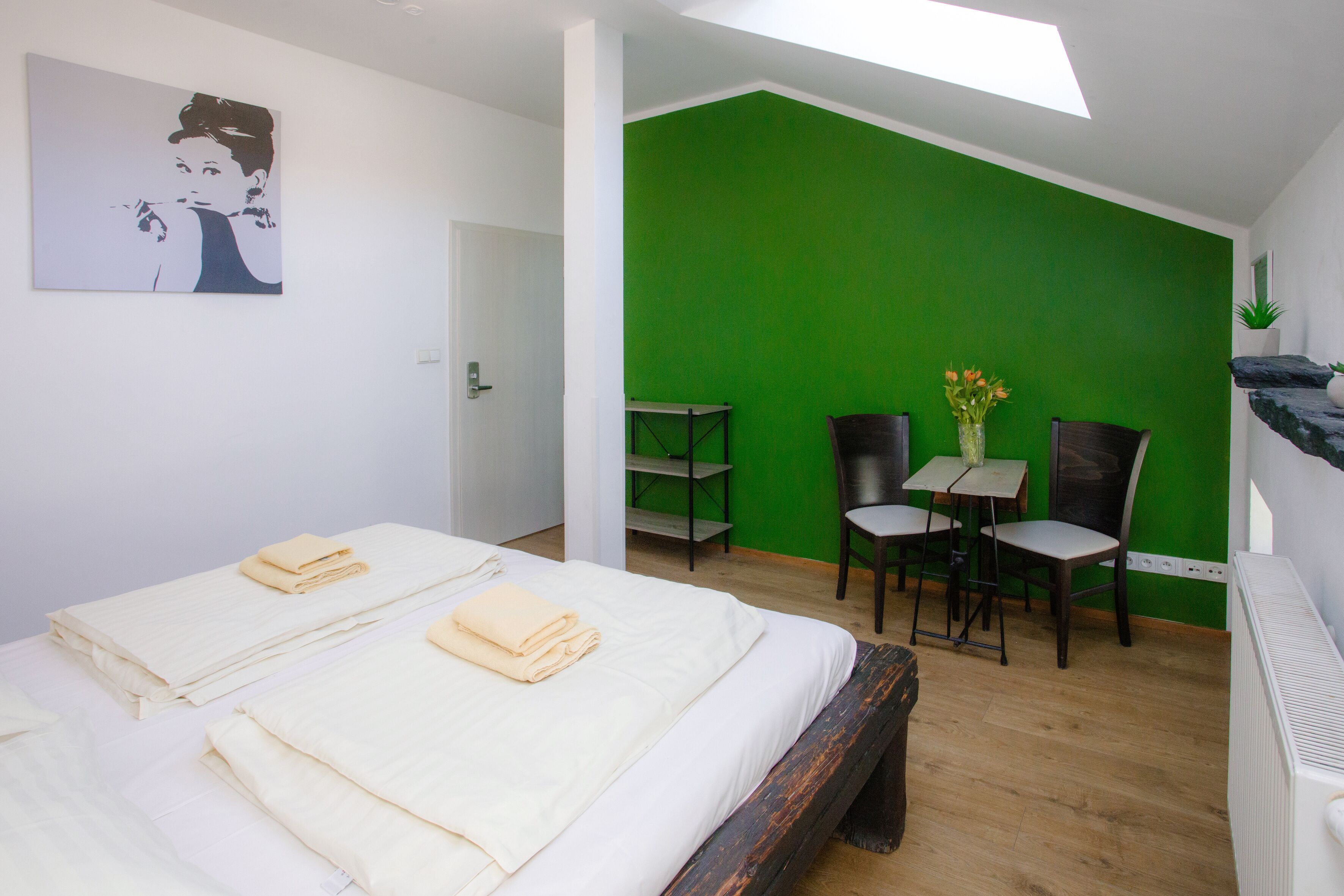 Ein Hotelzimmer mit zwei Betten, einer grünen Wand als Akzent, einem kleinen Tisch mit Stühlen und einem Gemälde an der Wand.