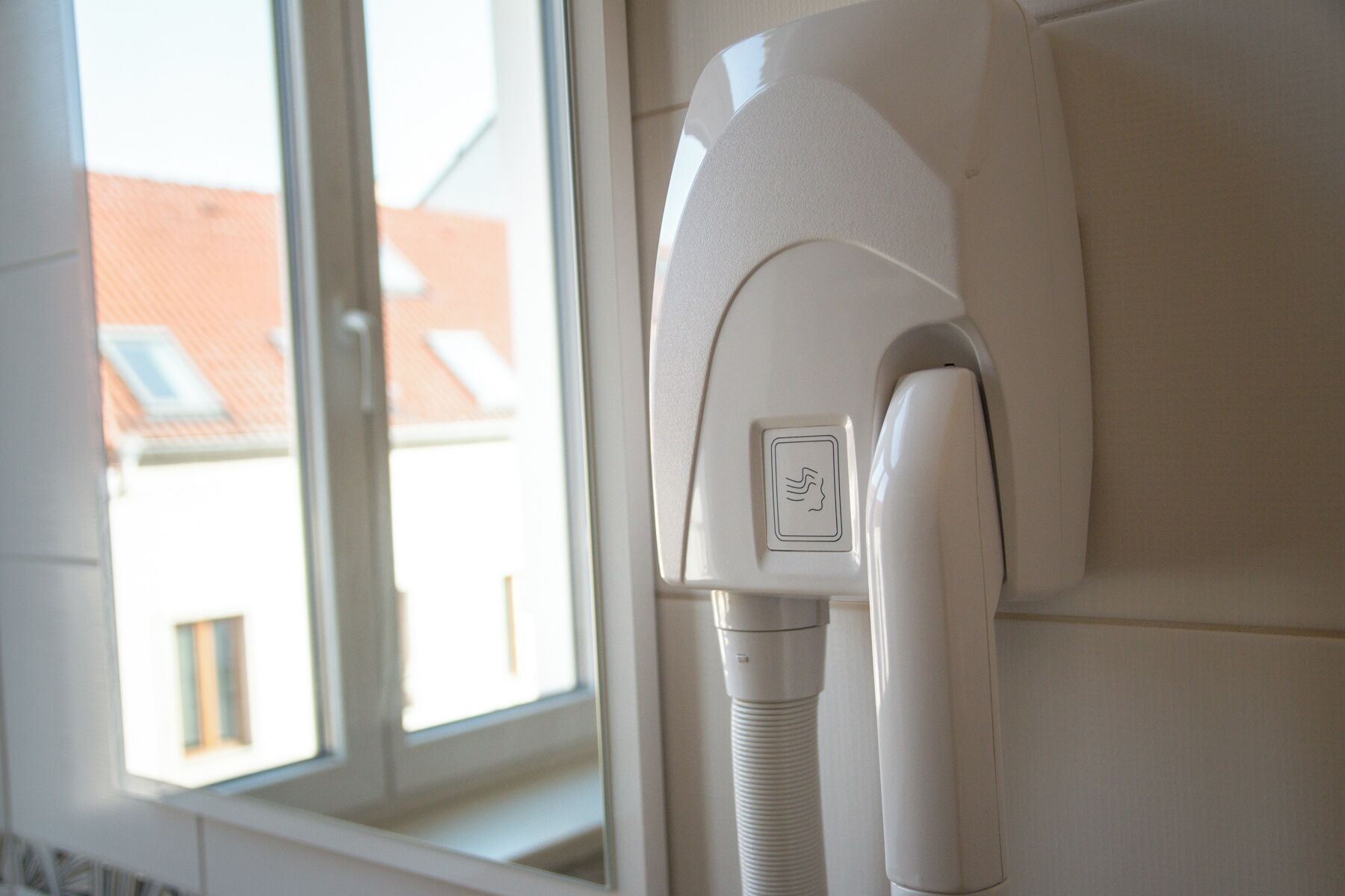 A hairdryer mounted on a wall near a window with a view of buildings outside.