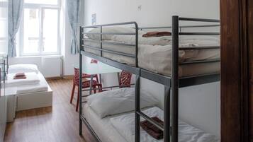 A bunk bed room with a desk and chair, a window with curtains, and a radiator.