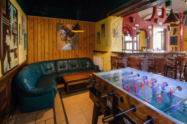 A bar area with a foosball table, wooden walls, and a green leather couch.