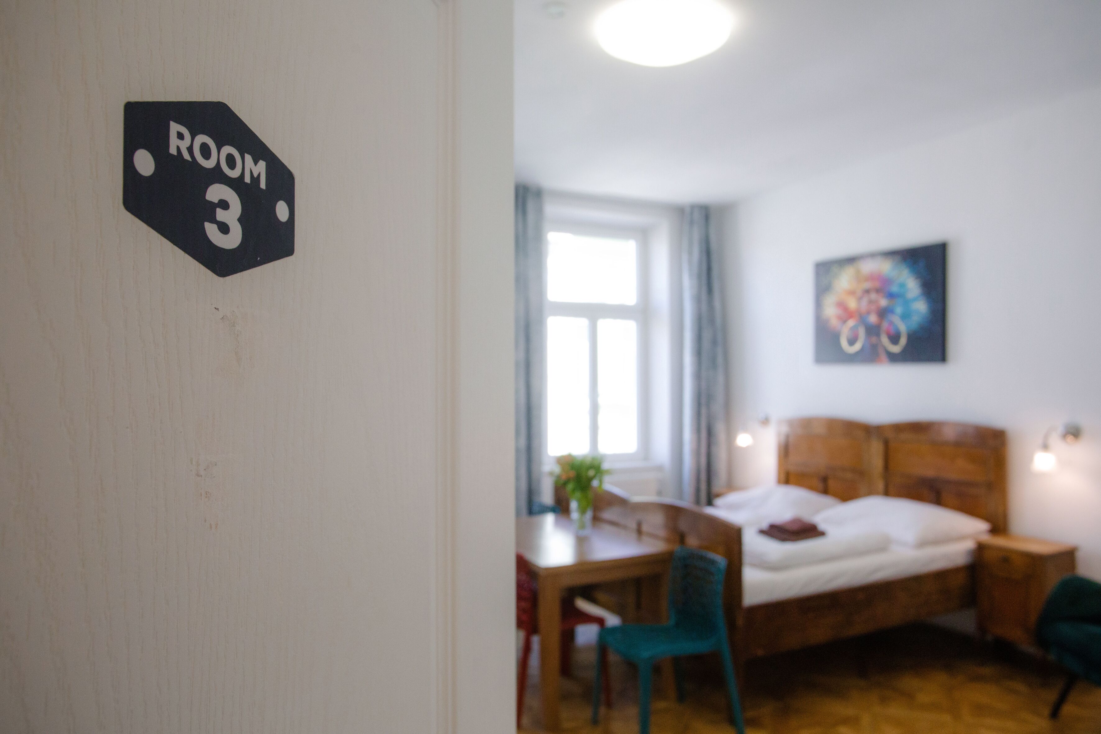 A room with a bed, a desk, a chair, and a painting on the wall.