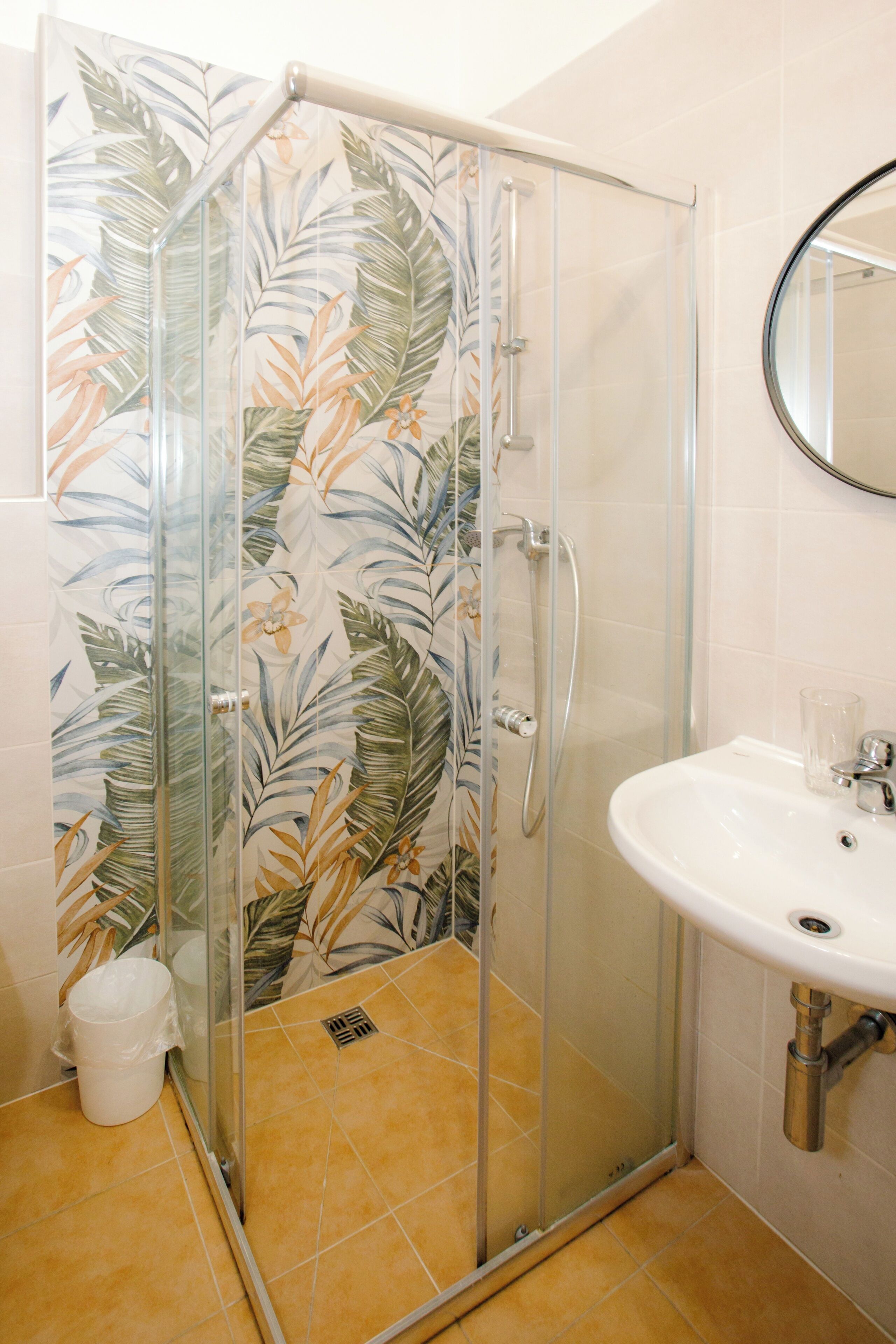 Una ducha con puerta de cristal, un lavabo blanco y un espejo.