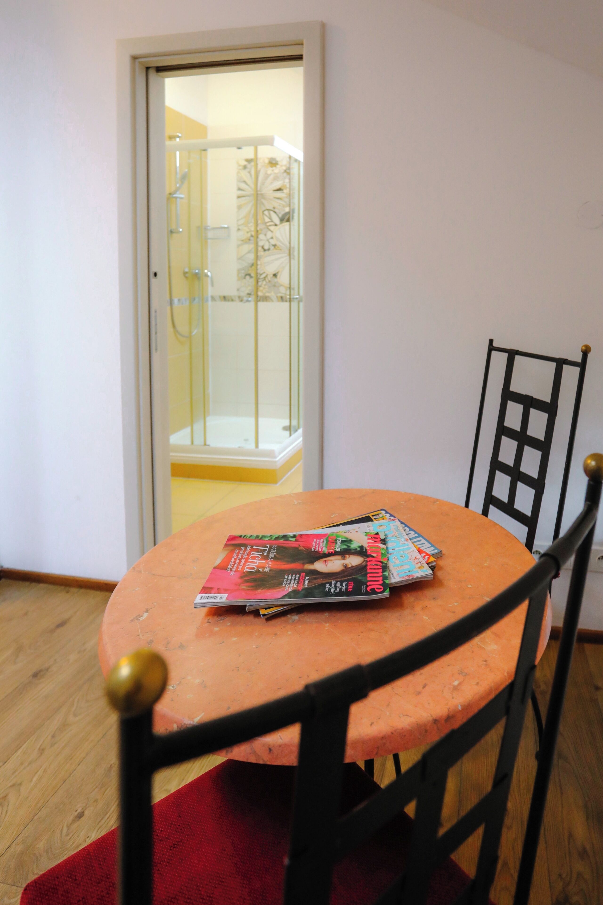 Quarto com uma mesa redonda, uma cadeira, uma porta que dá para um espaço com chuveiro e uma revista sobre a mesa.