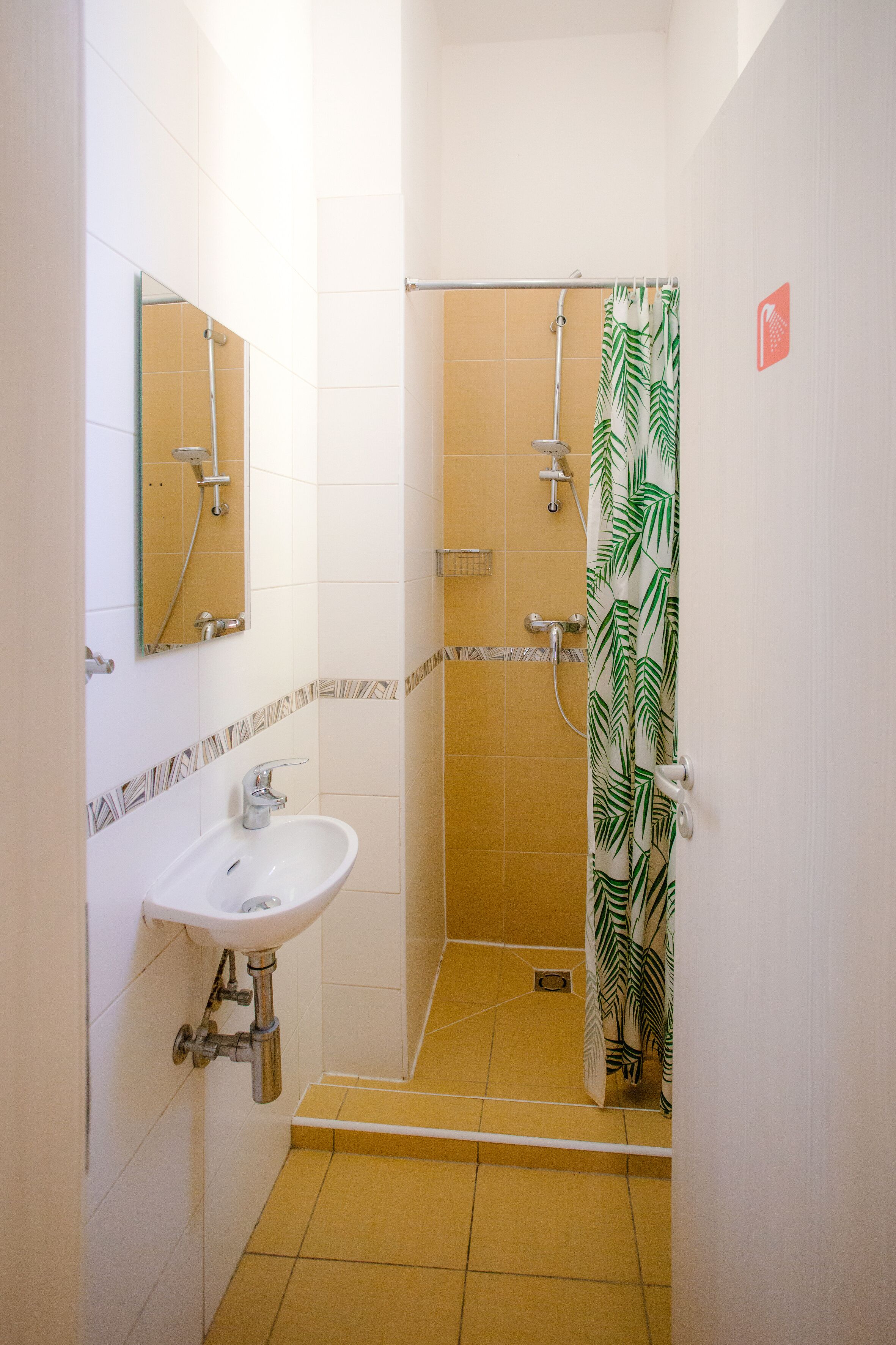 A bathroom with a sink, mirror, shower, and a patterned shower curtain.