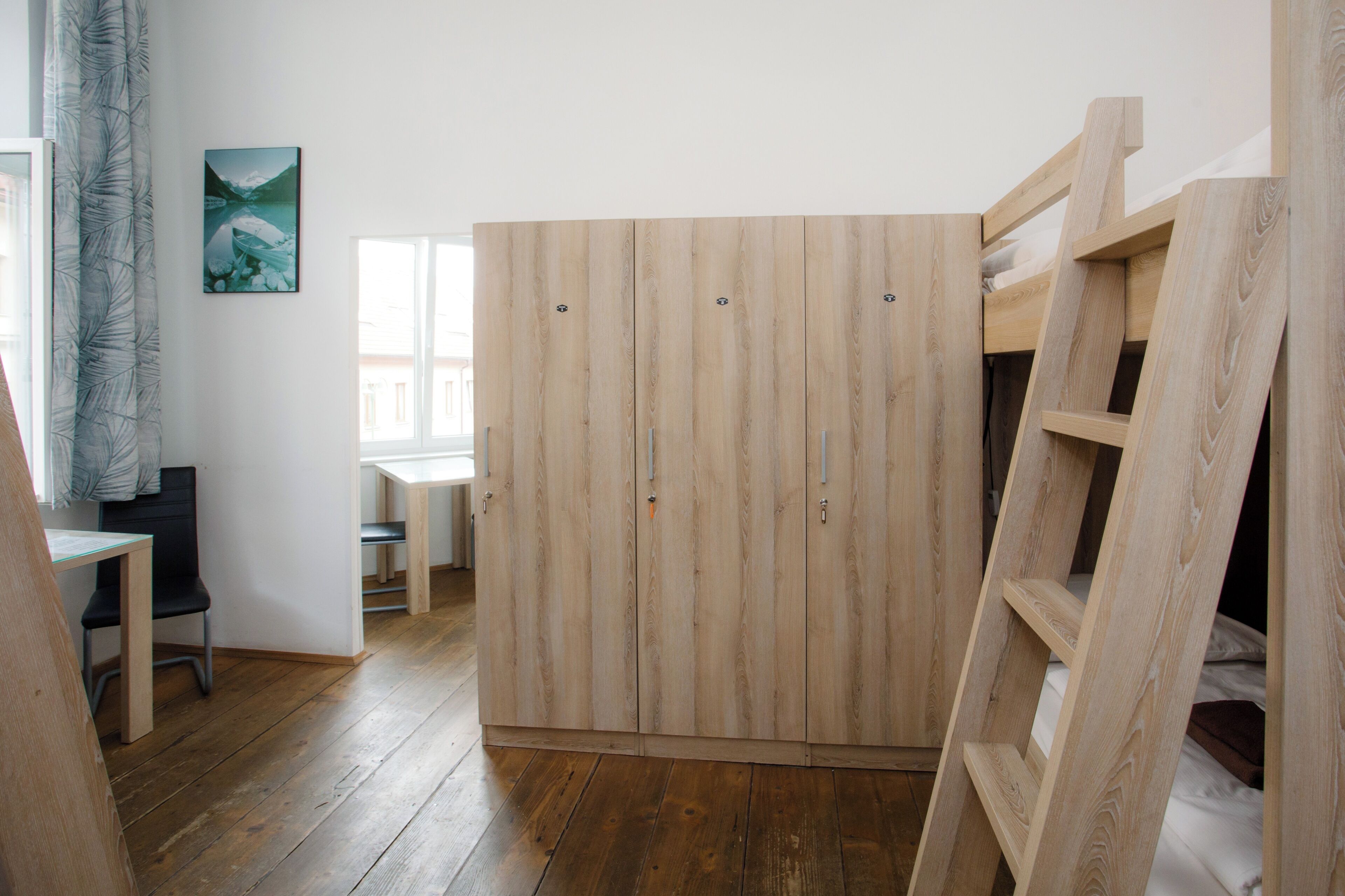 A room with a wooden wardrobe, a desk, a chair, and a ladder.