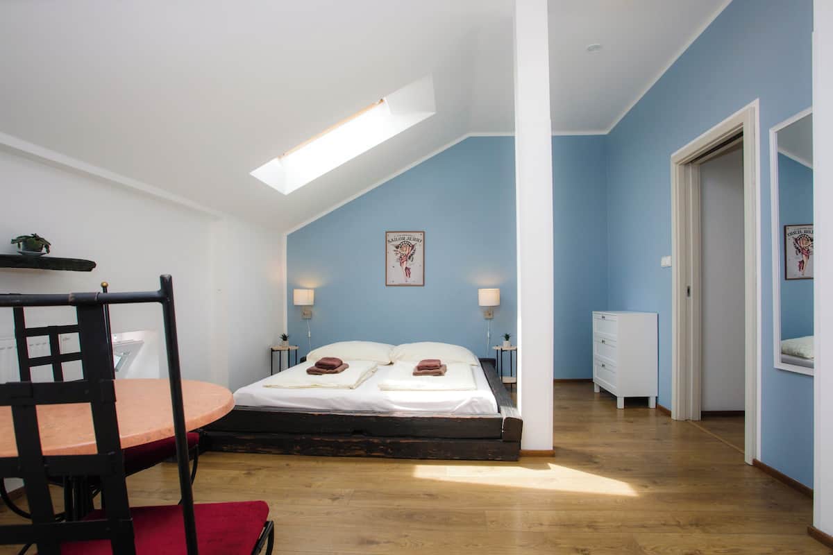 Ein Schlafzimmer mit Oberlicht, einem Bett mit Kissen, einem Nachttisch, einer Kommode und einem Stuhl.