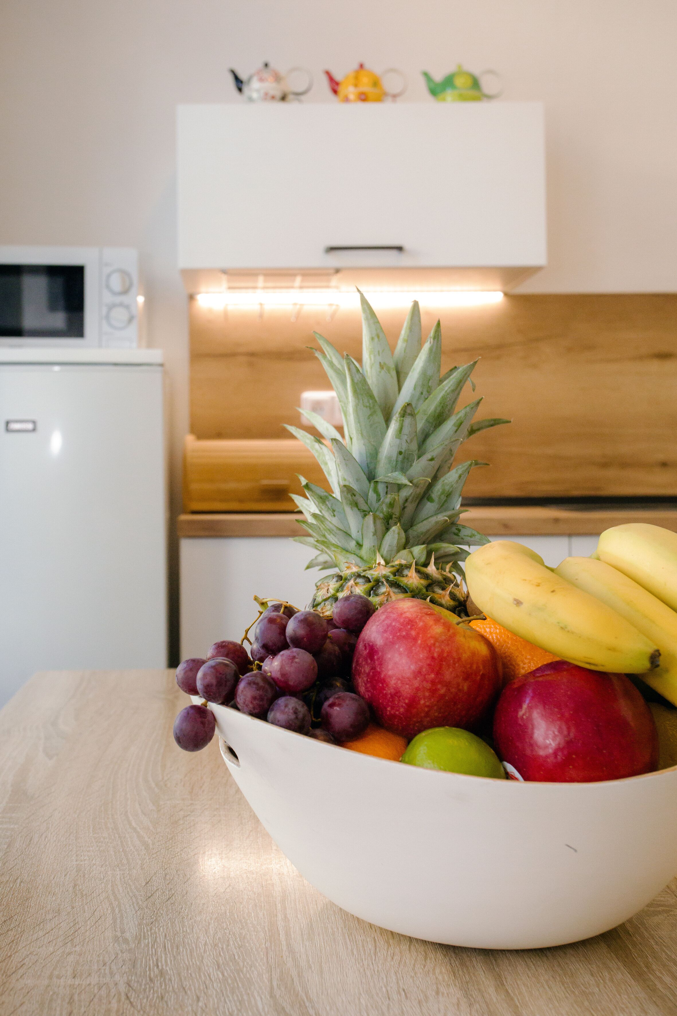 A white bowl with fruits on a wooden table in a kitchen.
