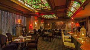 Un comedor con mesas y sillas, una zona de bar con taburetes y una estantería al fondo.