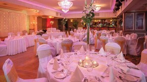 Un salón de banquetes con mesas redondas dispuestas para un evento formal, con manteles blancos, cubertería y centros de mesa florales.