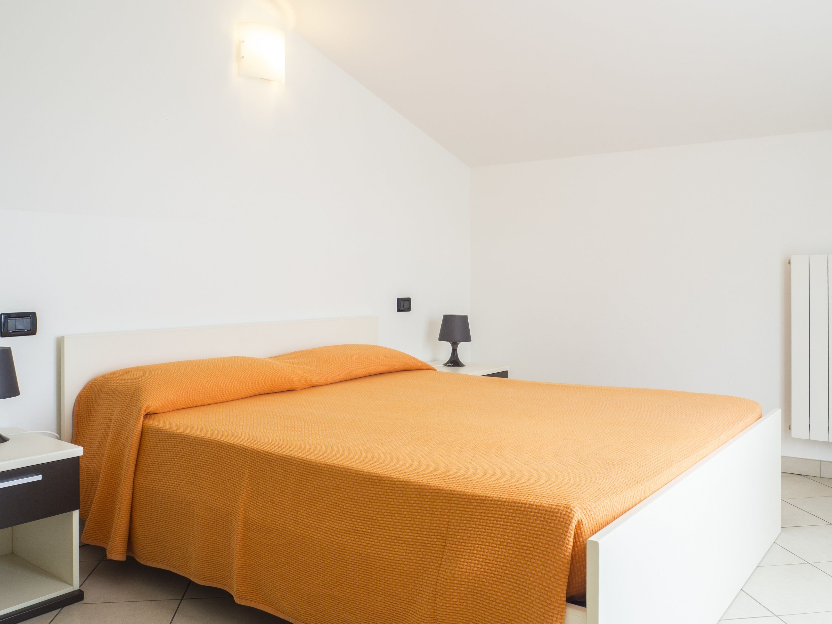 A bedroom with a bed, a nightstand, a lamp, and a wall-mounted light fixture.