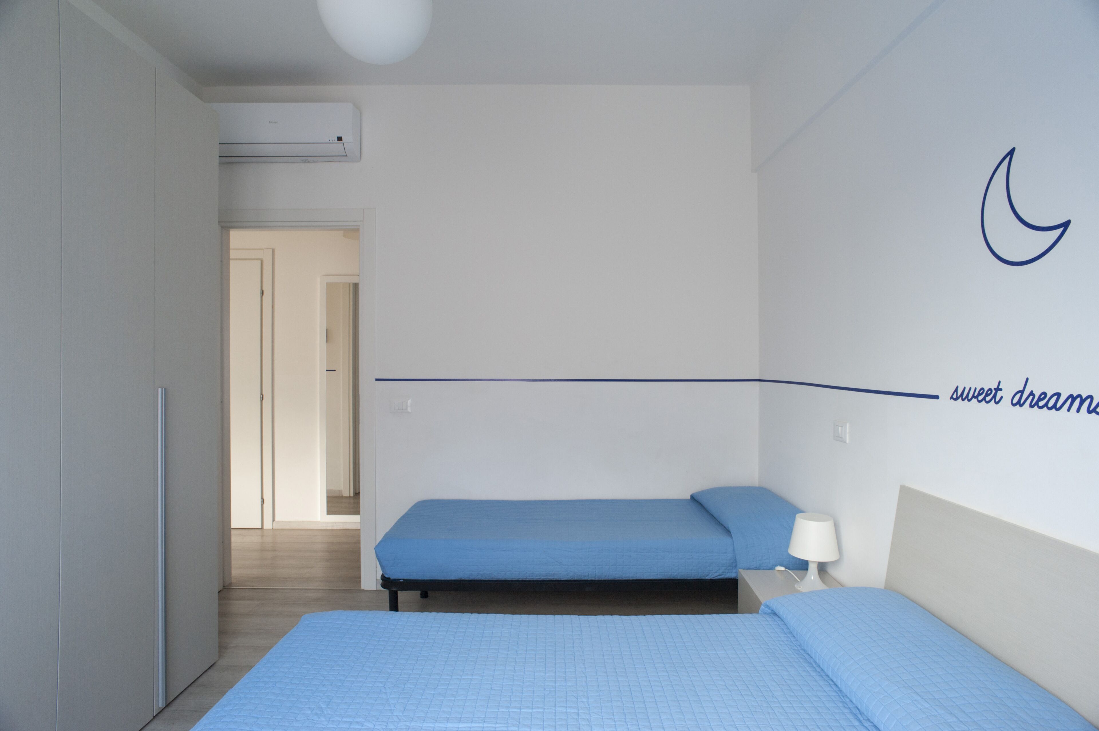A bedroom with two beds, a nightstand, and a wall-mounted air conditioner.
